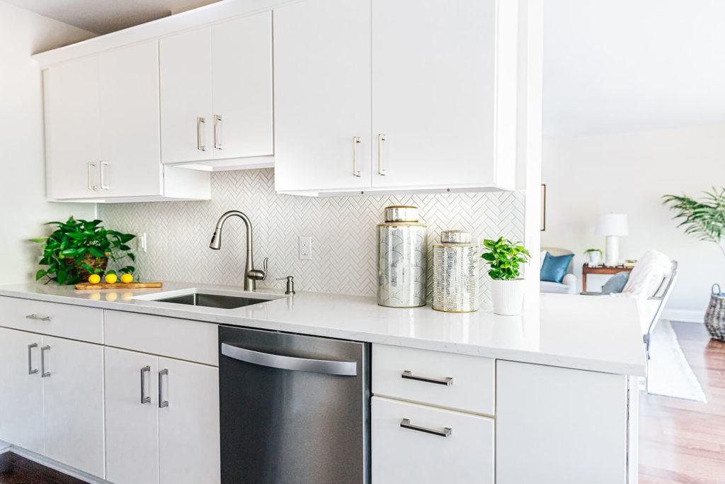 Updated white galley kitchen with brushed nickel hardware, dark wood floors, staged quartz countertops and art decor ginger jars